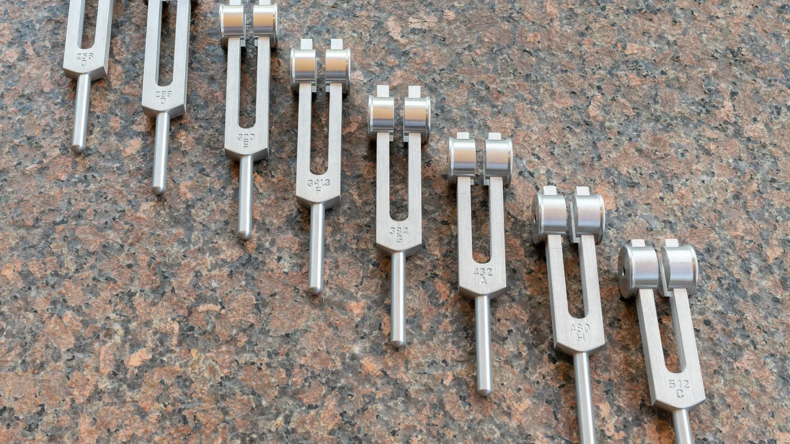 A row of tuning forks of different sizes on a stone surface