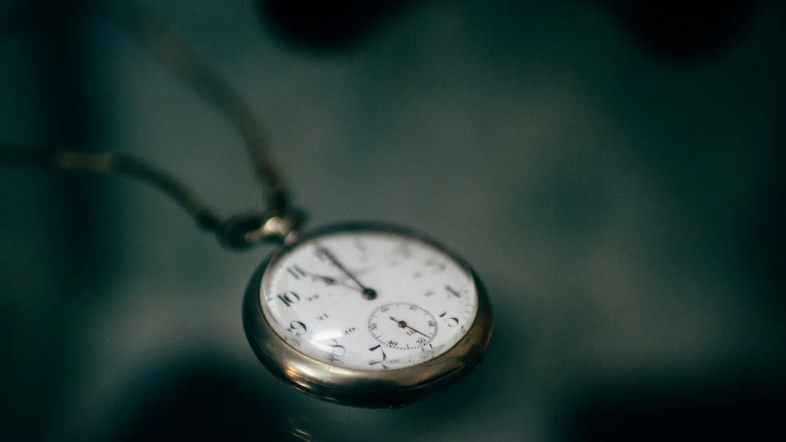 A silver pocket watch hanging on a chain against a dark background