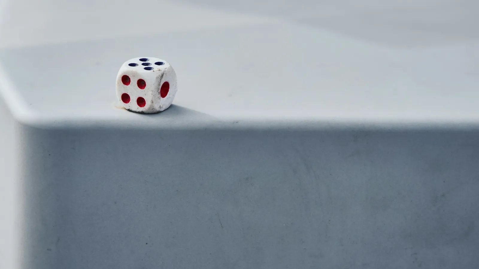 A single die resting on the edge of a grey surface