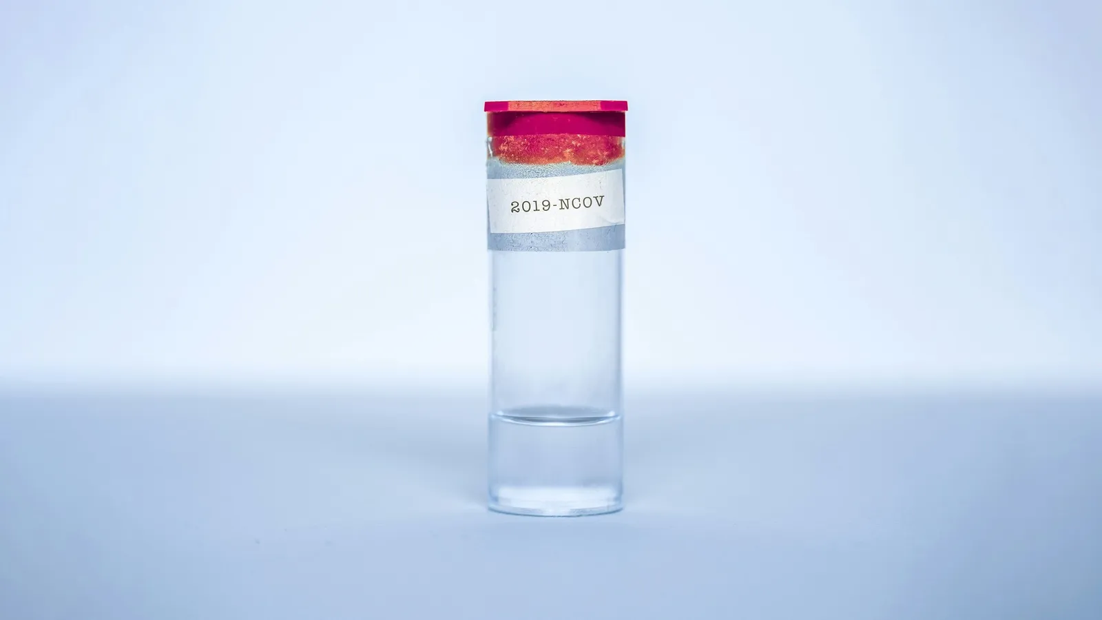A small glass vial with a red cap against a blue background