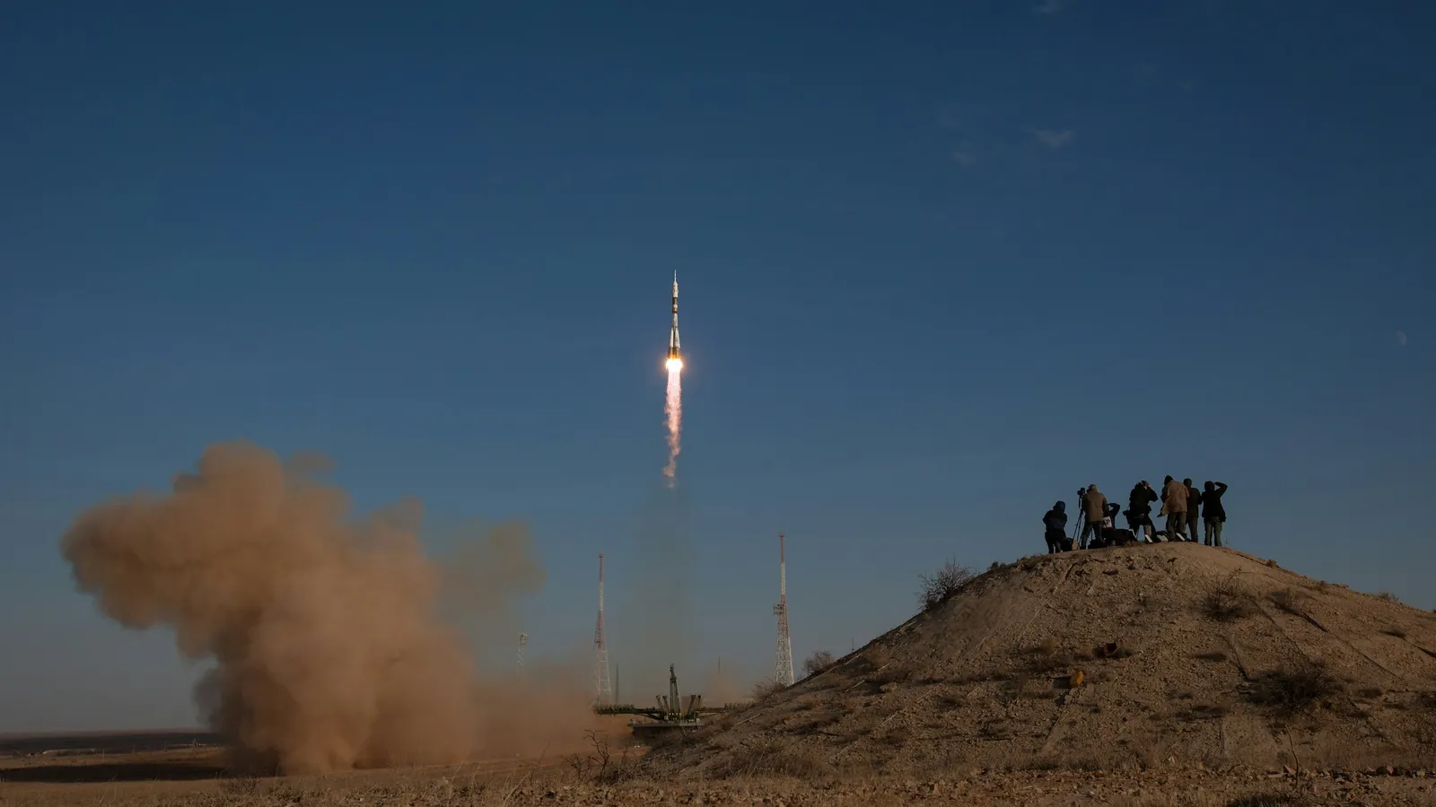 A small rocket lifting off as people watch from a nearby hilltop