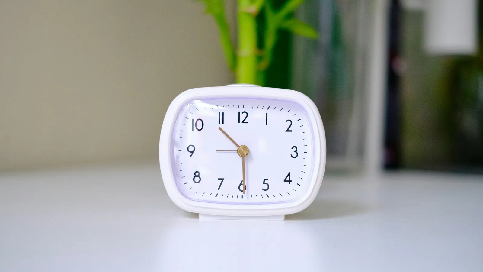 A small white alarm clock on a white table