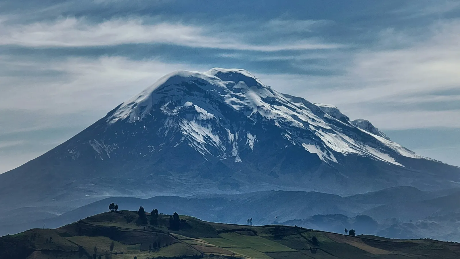 A snow-capped volcano rising above green highlands
