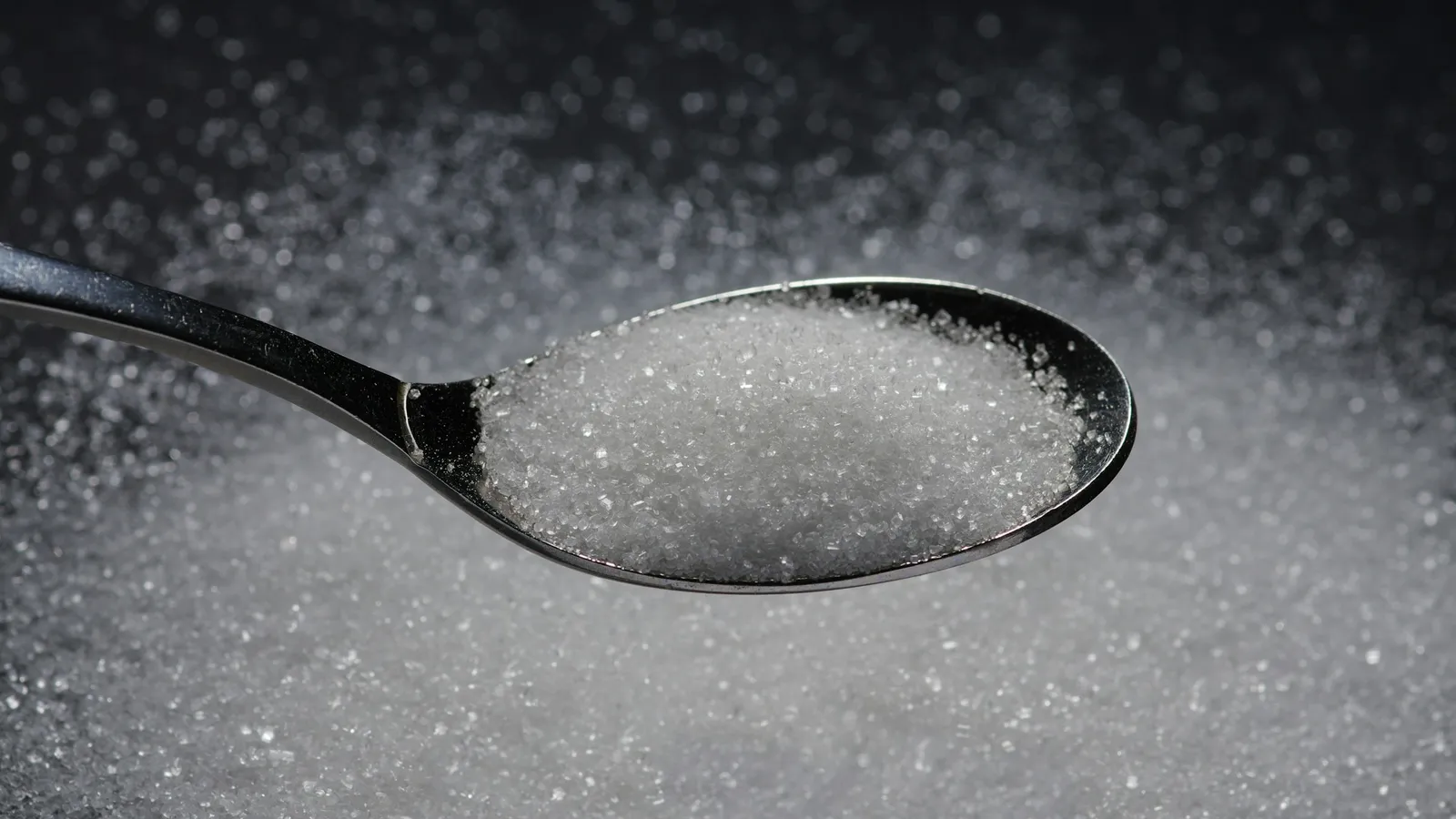 A spoonful of white sugar above a heap of sugar