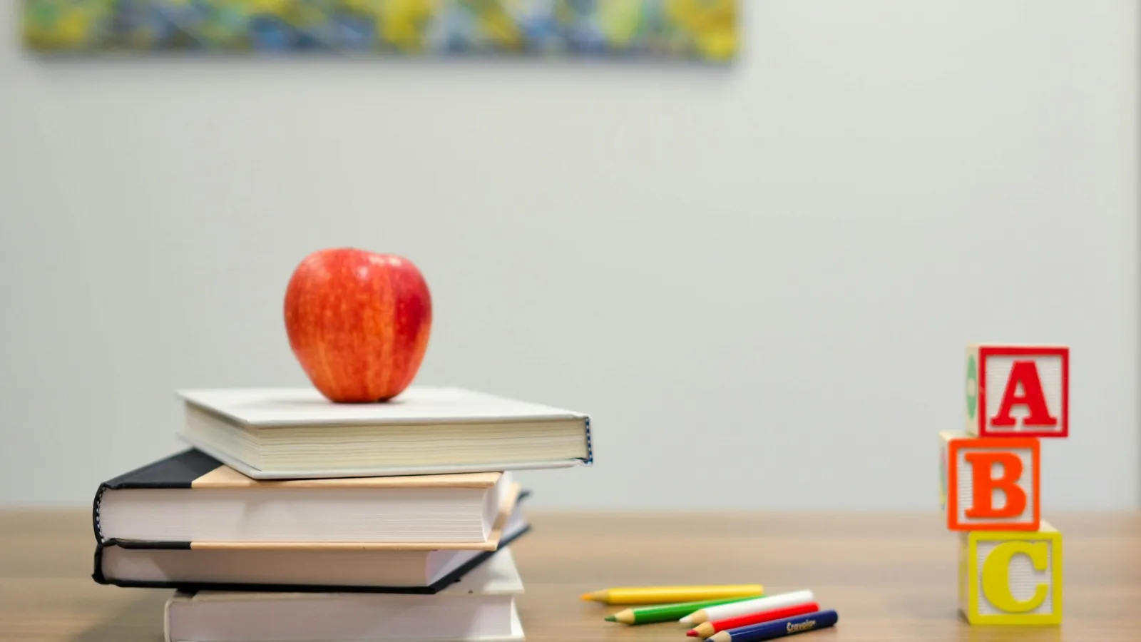 A stack of books with an apple and alphabet blocks on a desk