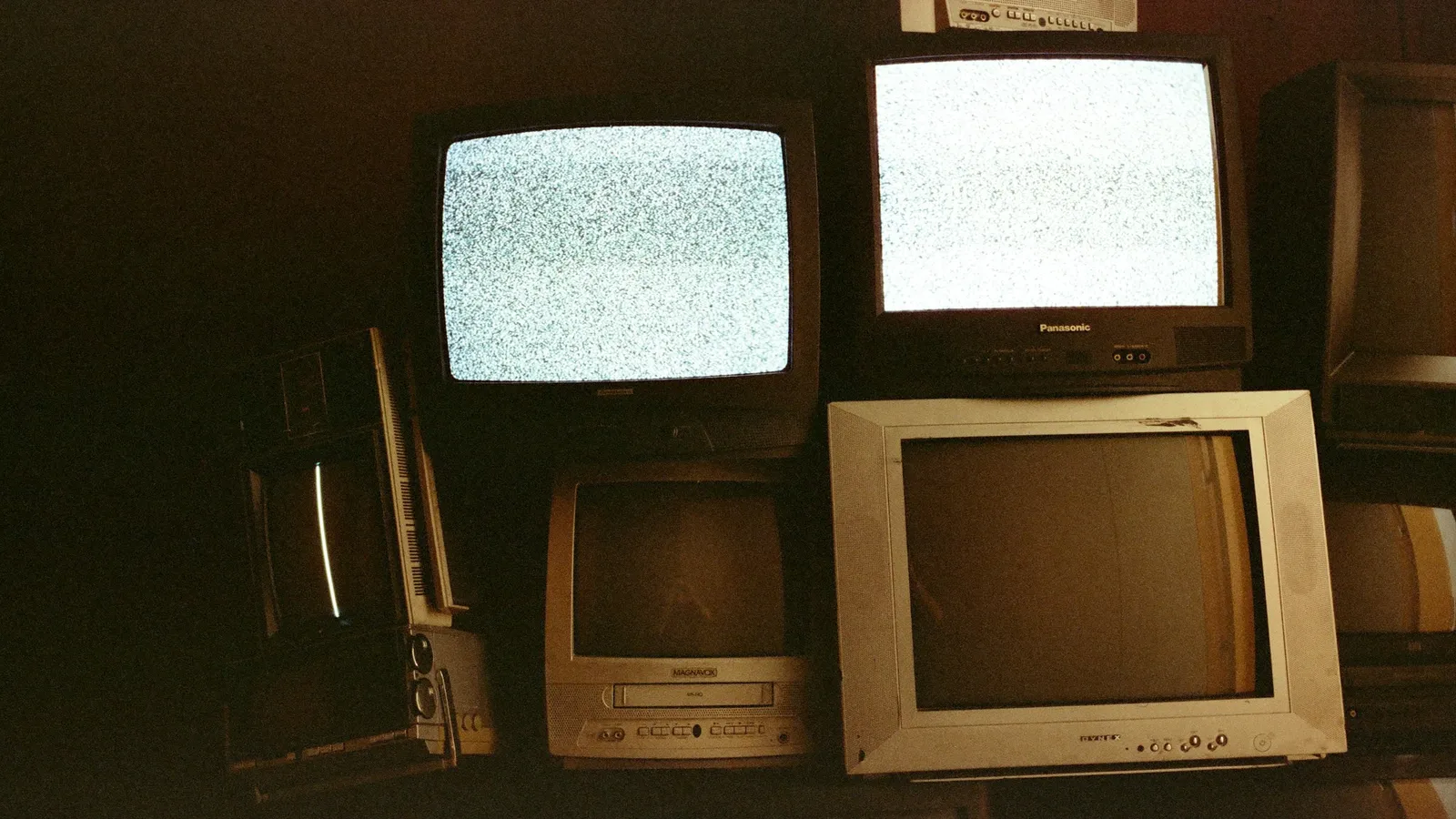 A stack of old computer monitors glowing in a dim room