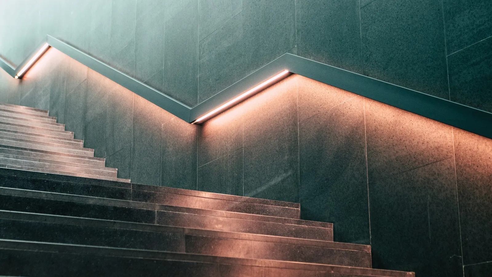 A staircase stepping up beside a lit handrail