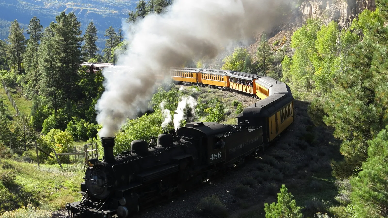 A steam locomotive puffing smoke through green hills
