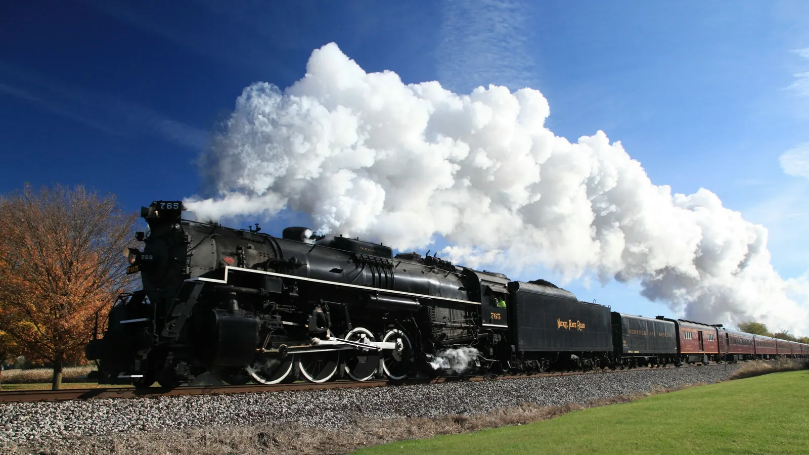 A steam locomotive puffing white smoke under a blue sky