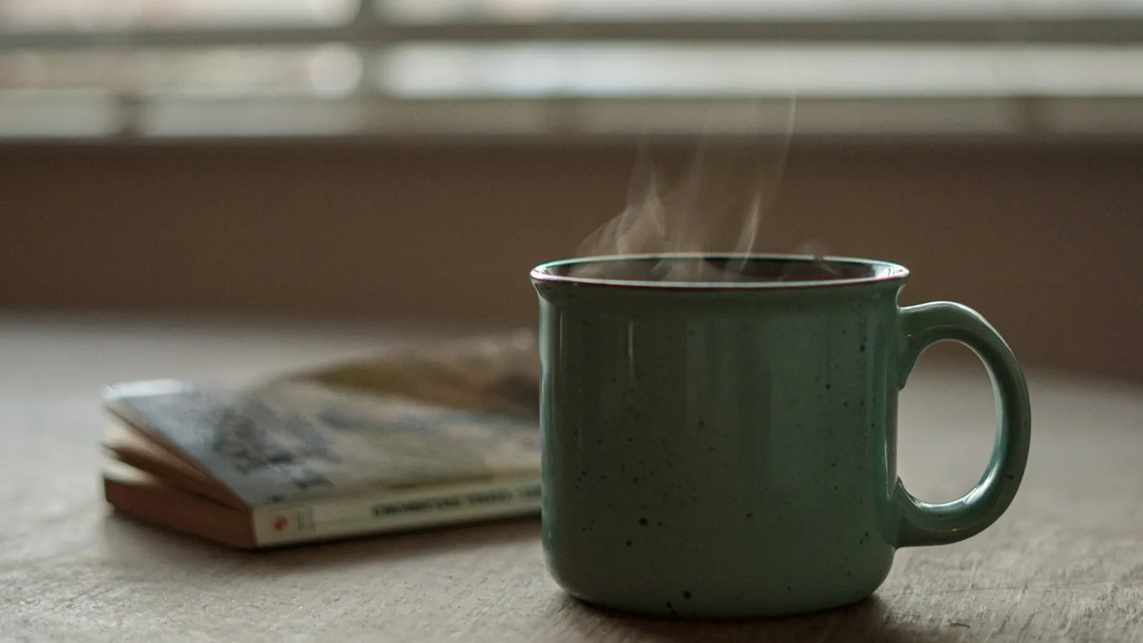 A steaming mug of tea on a table by a window
