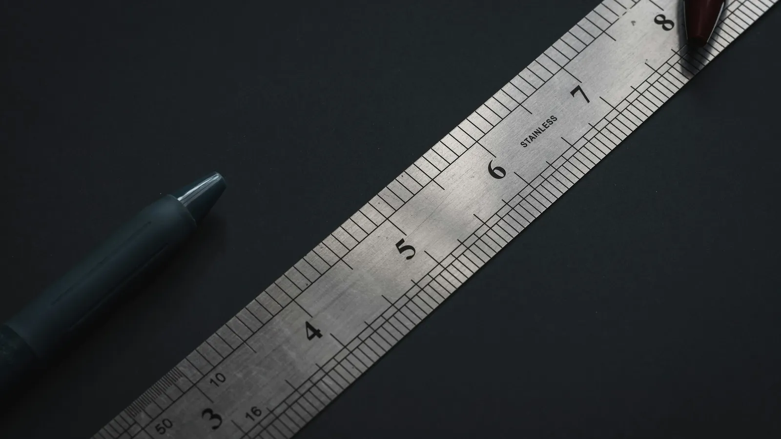 A steel ruler and pen on a dark surface