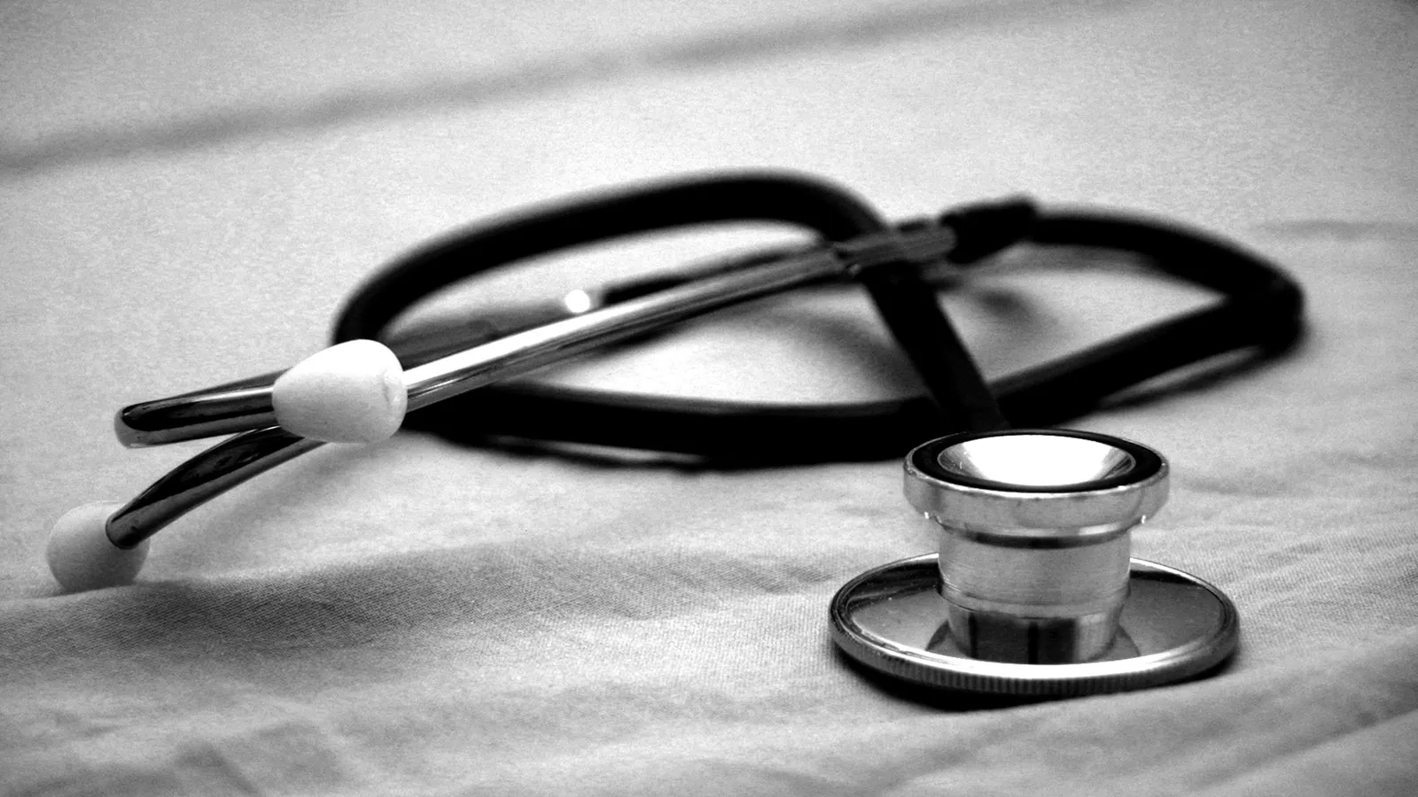 A stethoscope lying on a white surface, in black and white