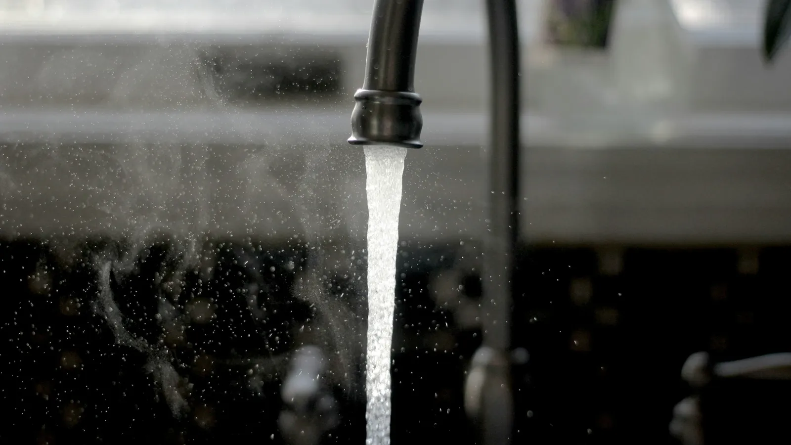 A stream of water falling from a metal tap against a dark background