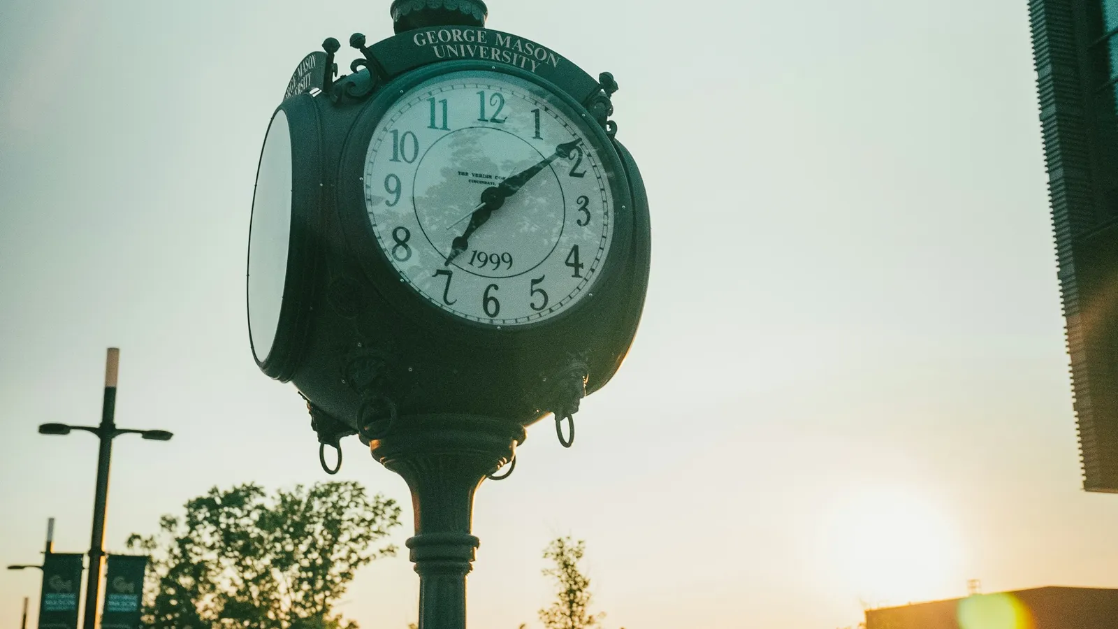 A street clock on a post with the sun low behind it