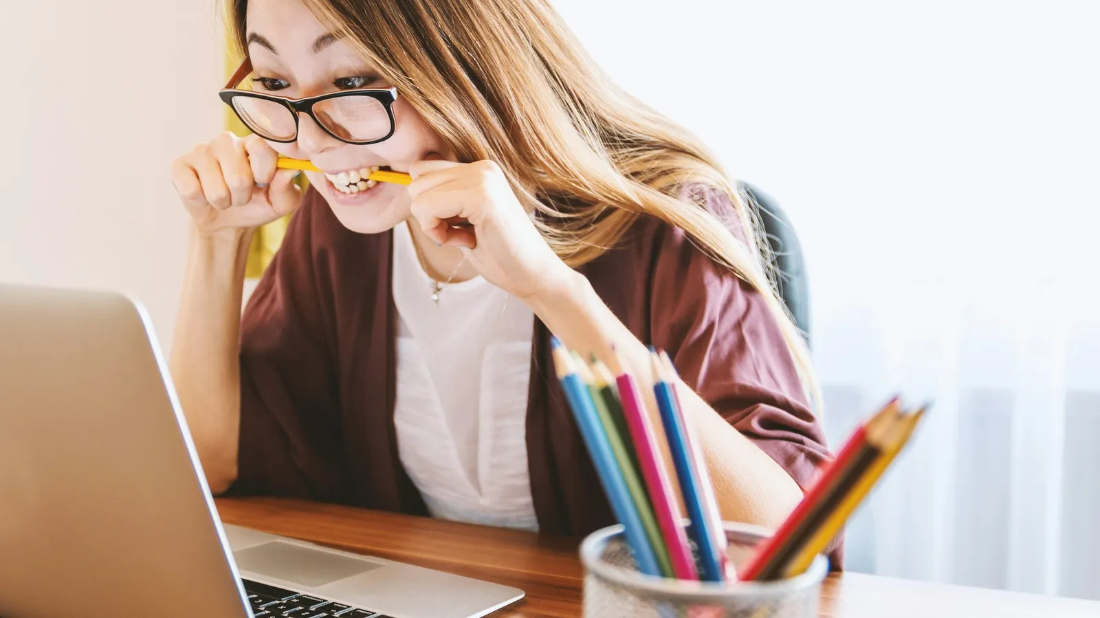 A student biting a pencil while staring at a laptop