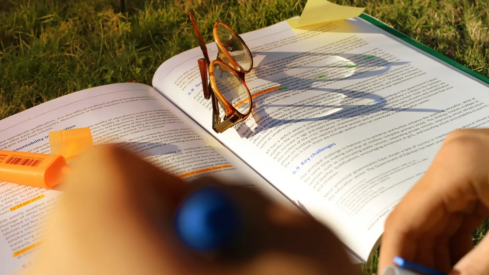 A student highlighting notes in an open book outdoors