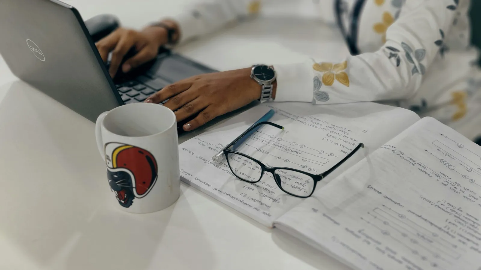 A student types at a laptop beside a notebook of handwritten working