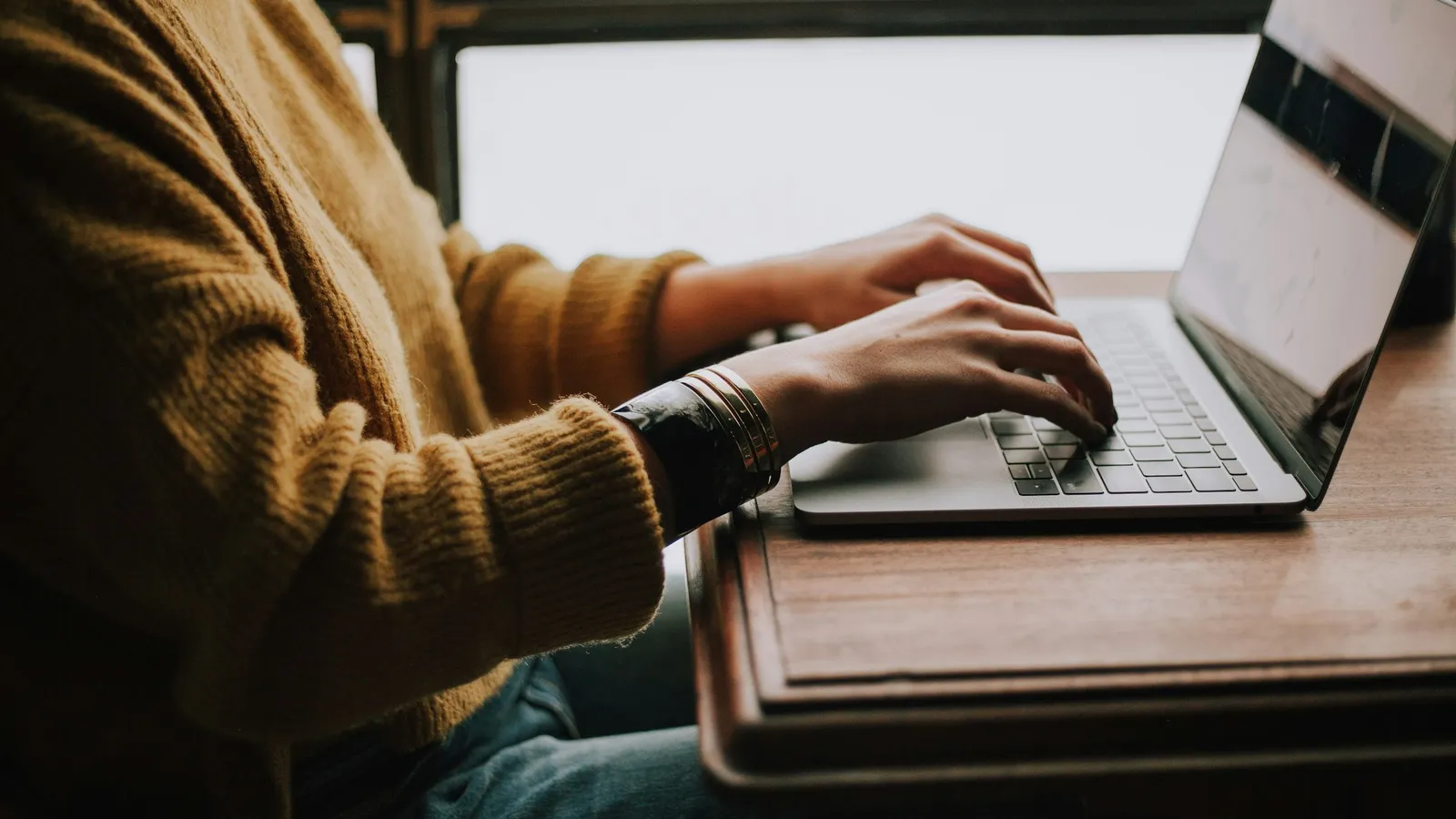 A student working on a laptop at a wooden desk