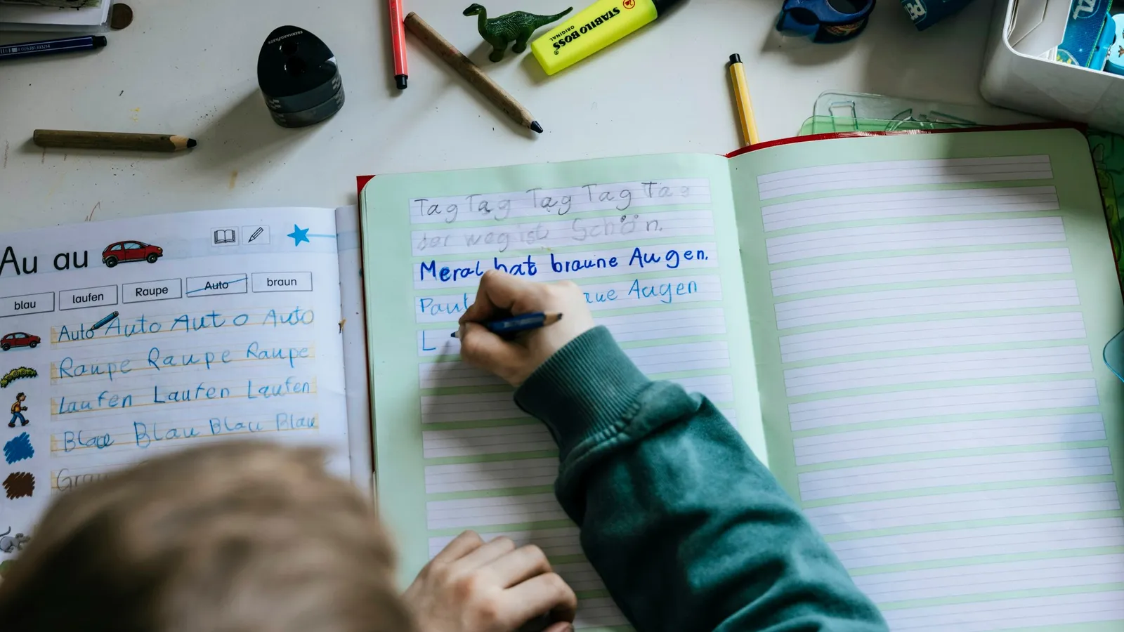 A student writing in an open notebook at a cluttered desk