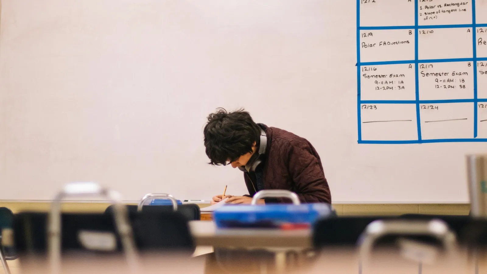 A student writing on paper at a desk in a classroom