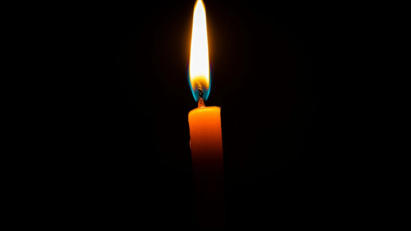 A tall candle flame burning in the dark