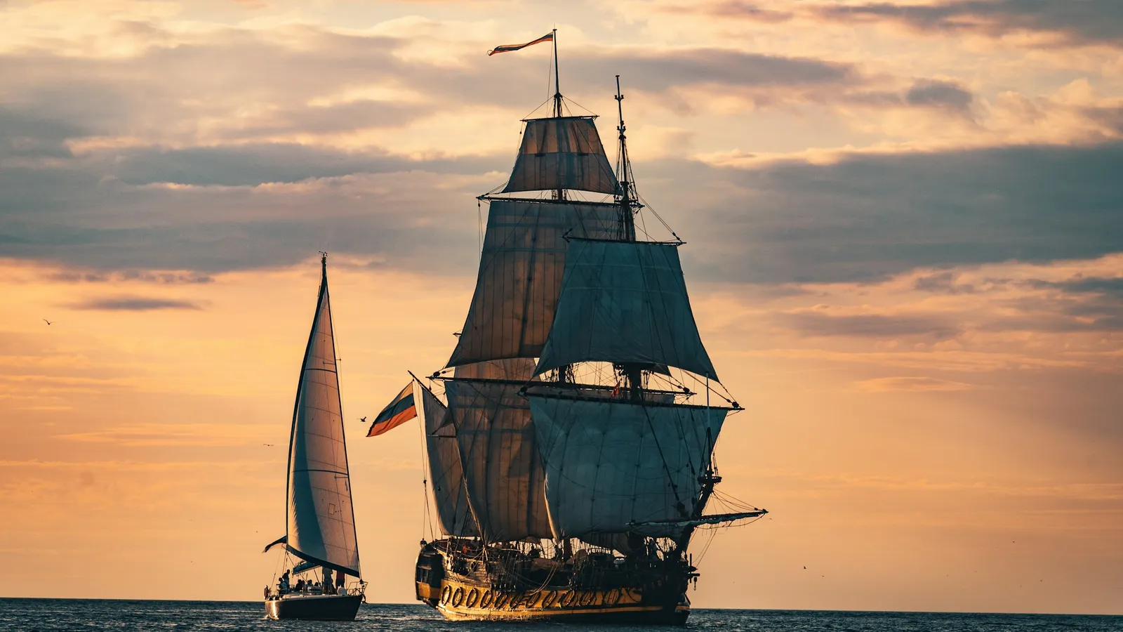A tall sailing ship at sea at sunset