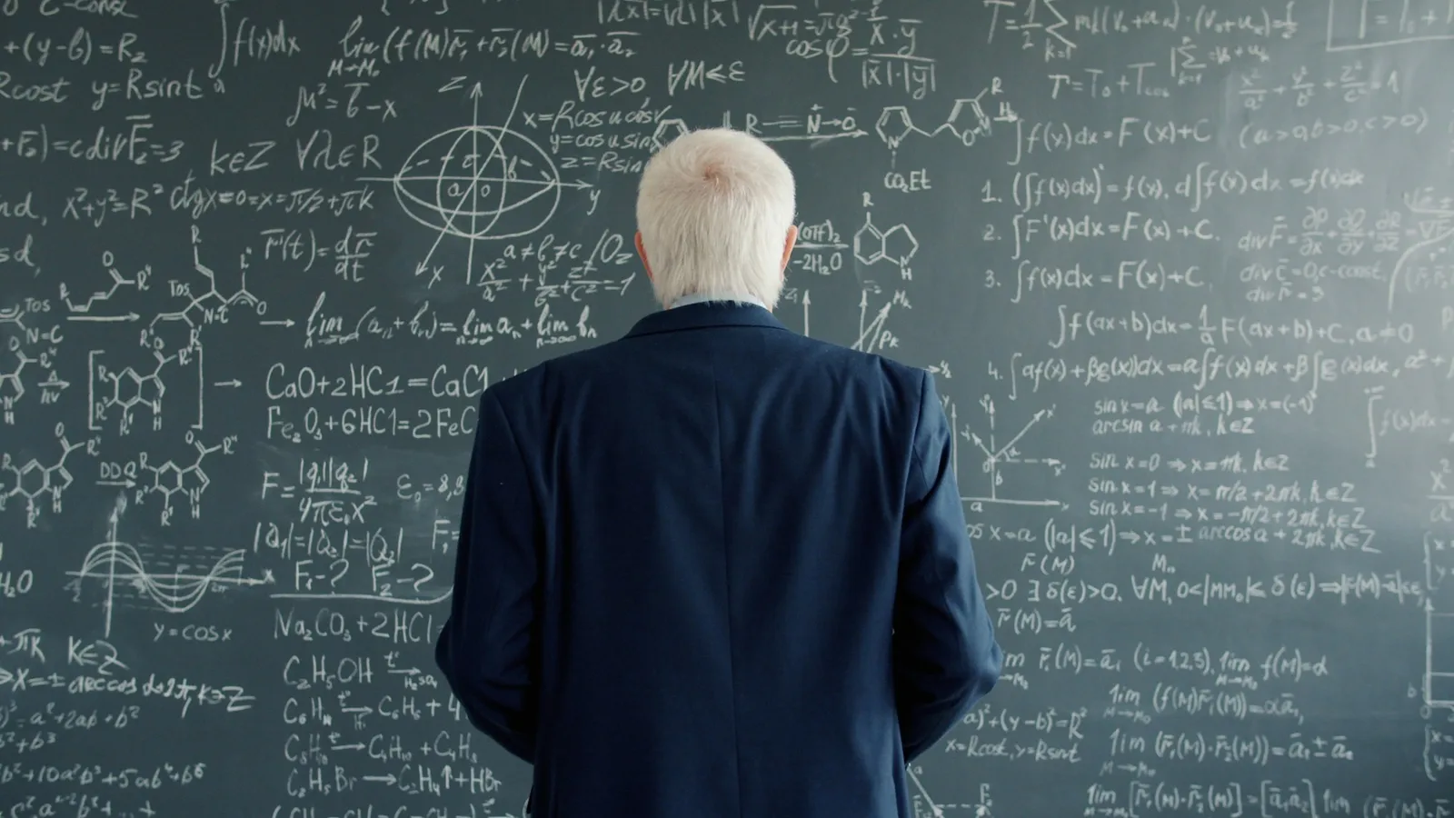 A teacher facing a chalkboard full of equations