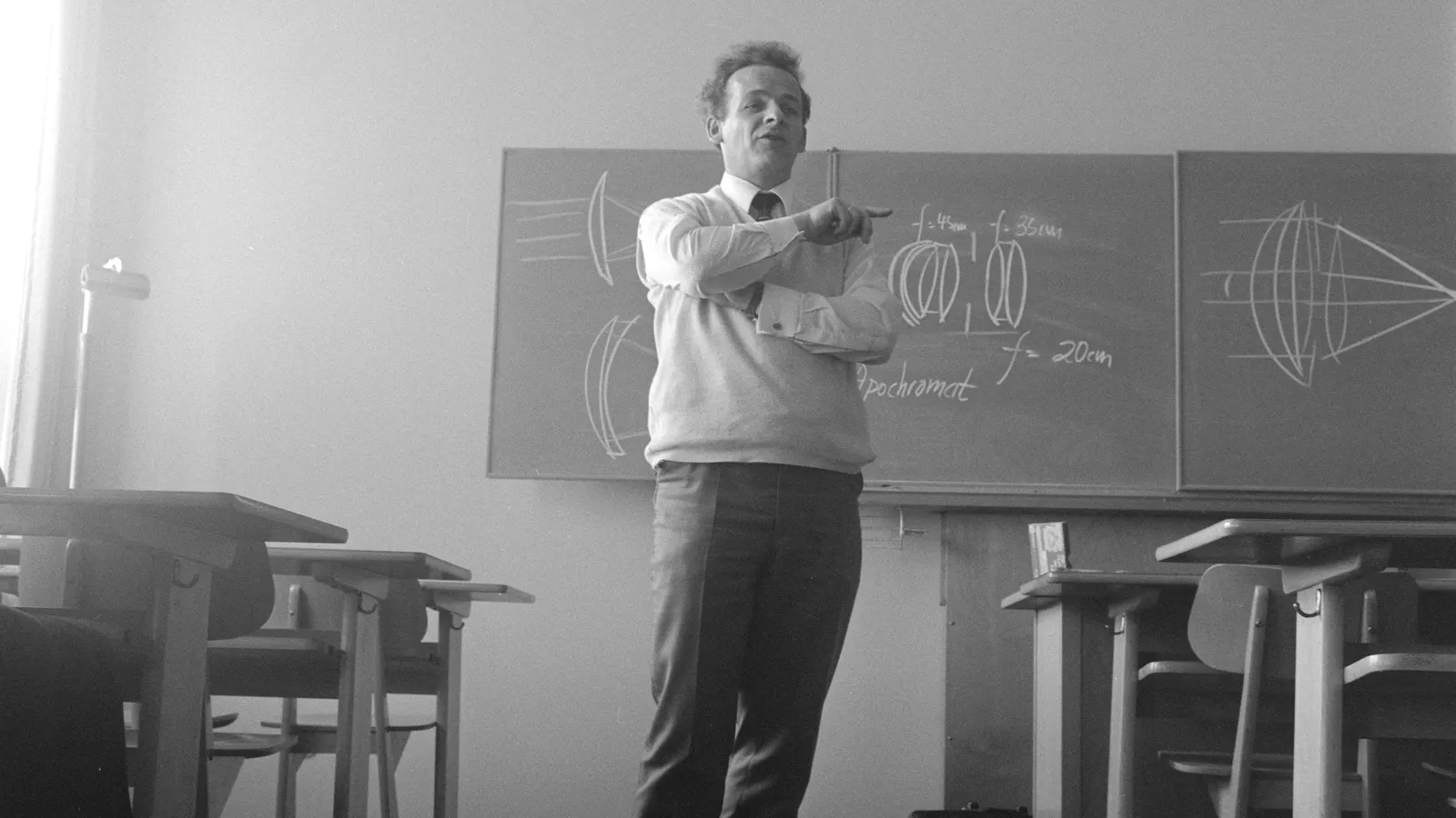 A teacher standing in front of a blackboard, in black and white
