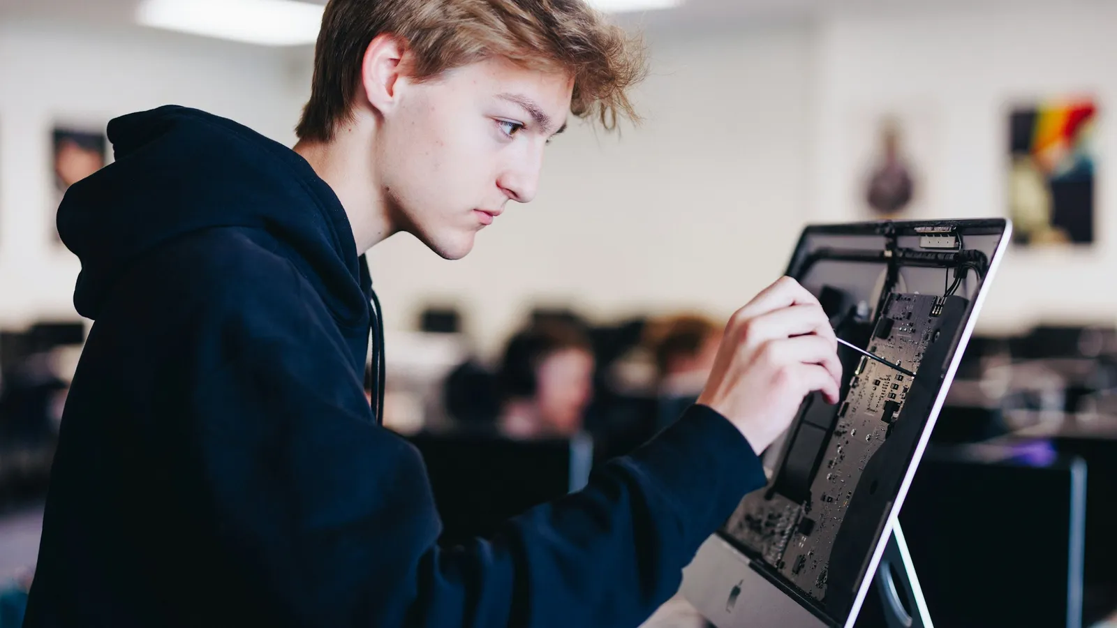 A teenage student draws on a large touchscreen in a classroom
