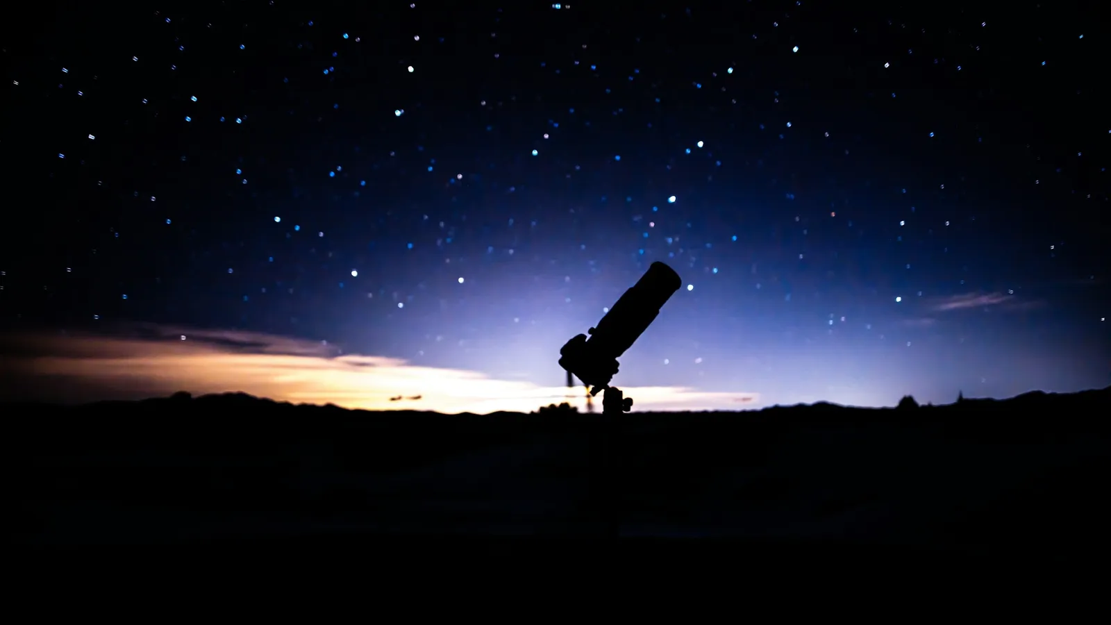 A telescope silhouetted against a starry twilight sky