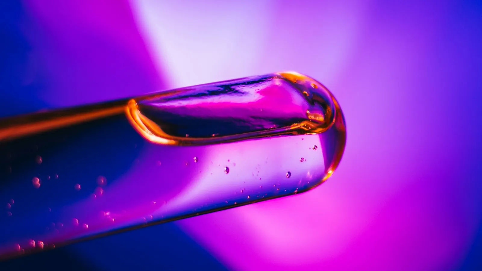A test tube holding a drop of liquid in pink light