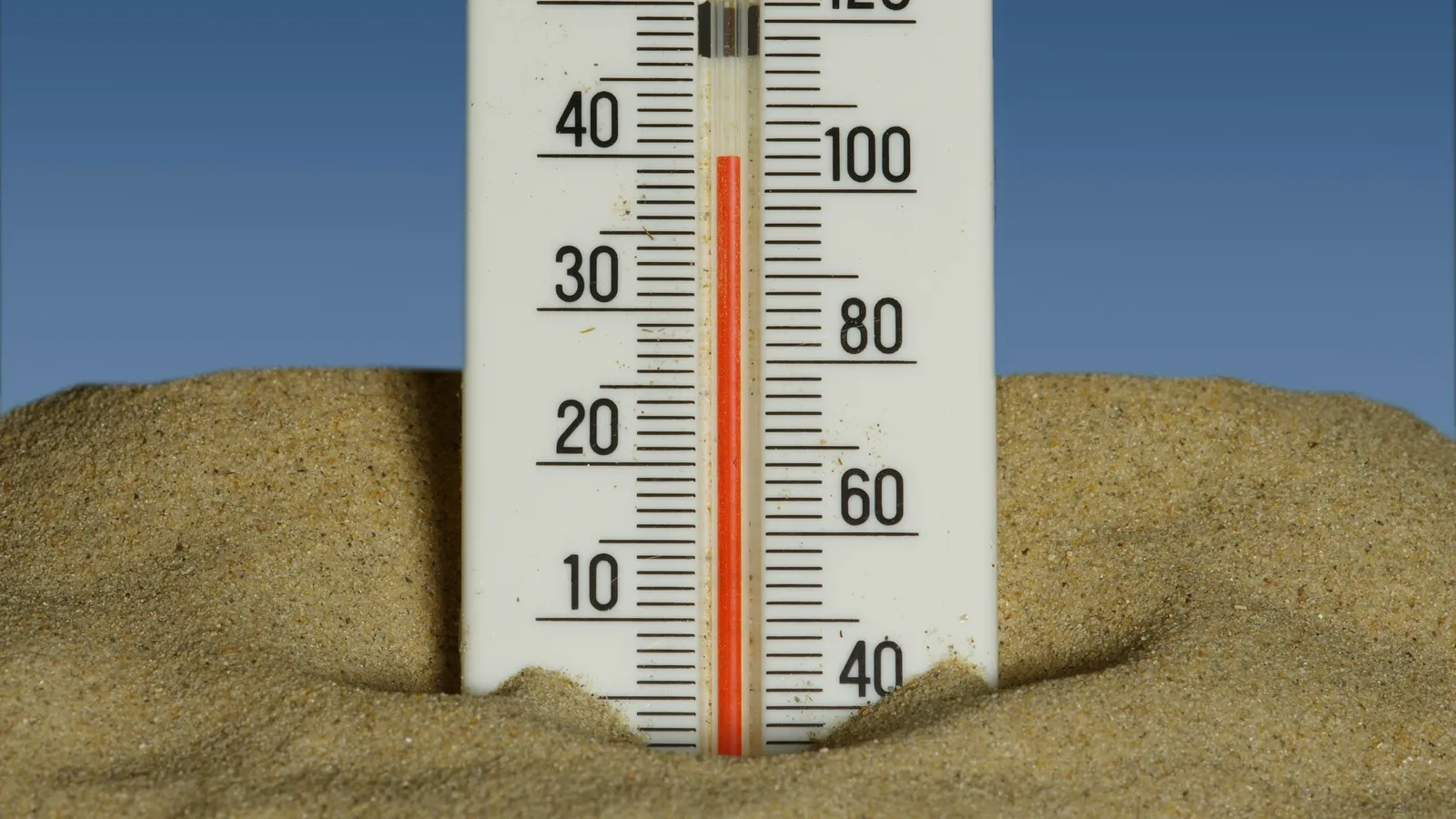 A thermometer standing in sand under a blue sky