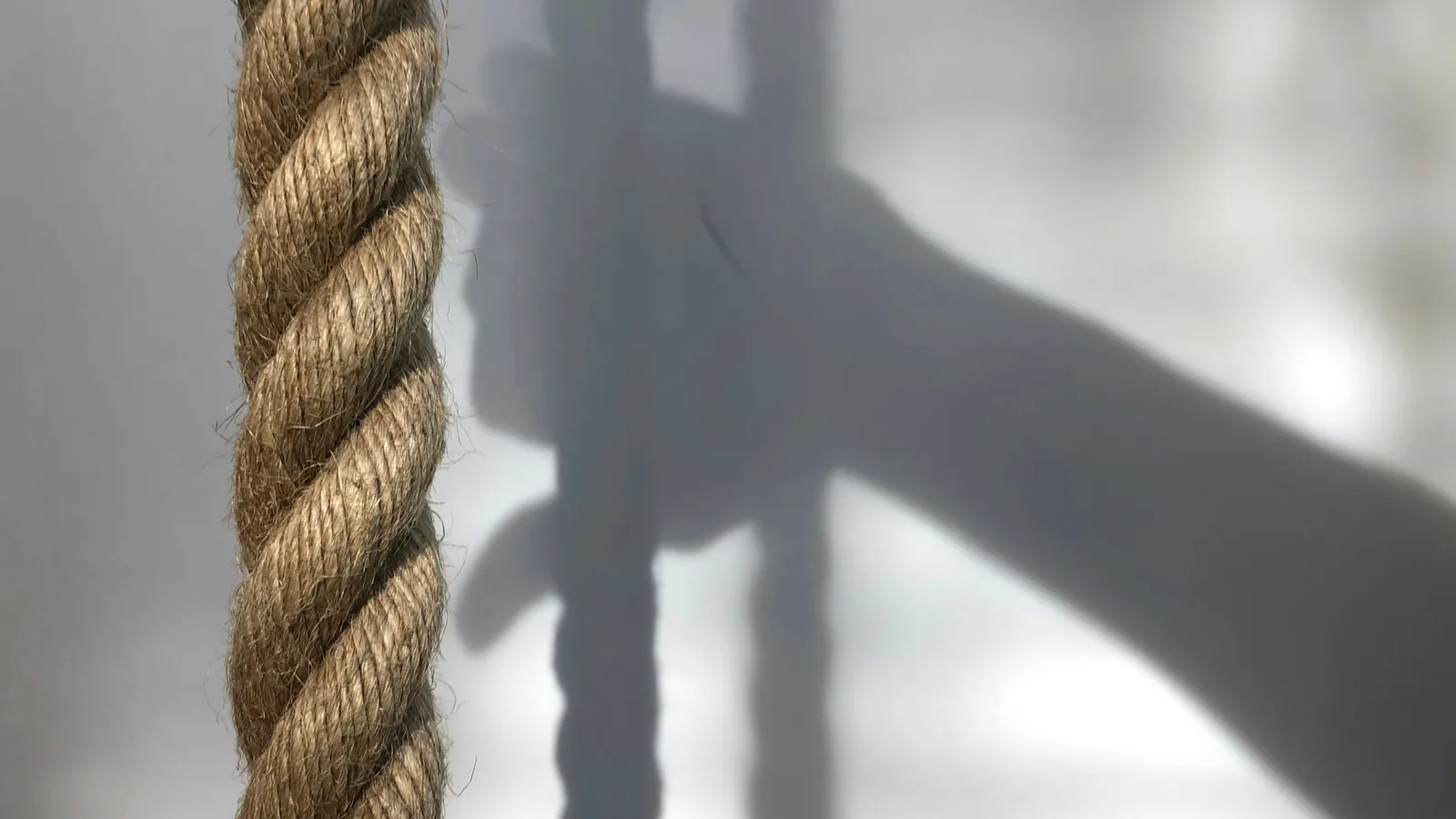 A thick rope hanging straight down beside a wall