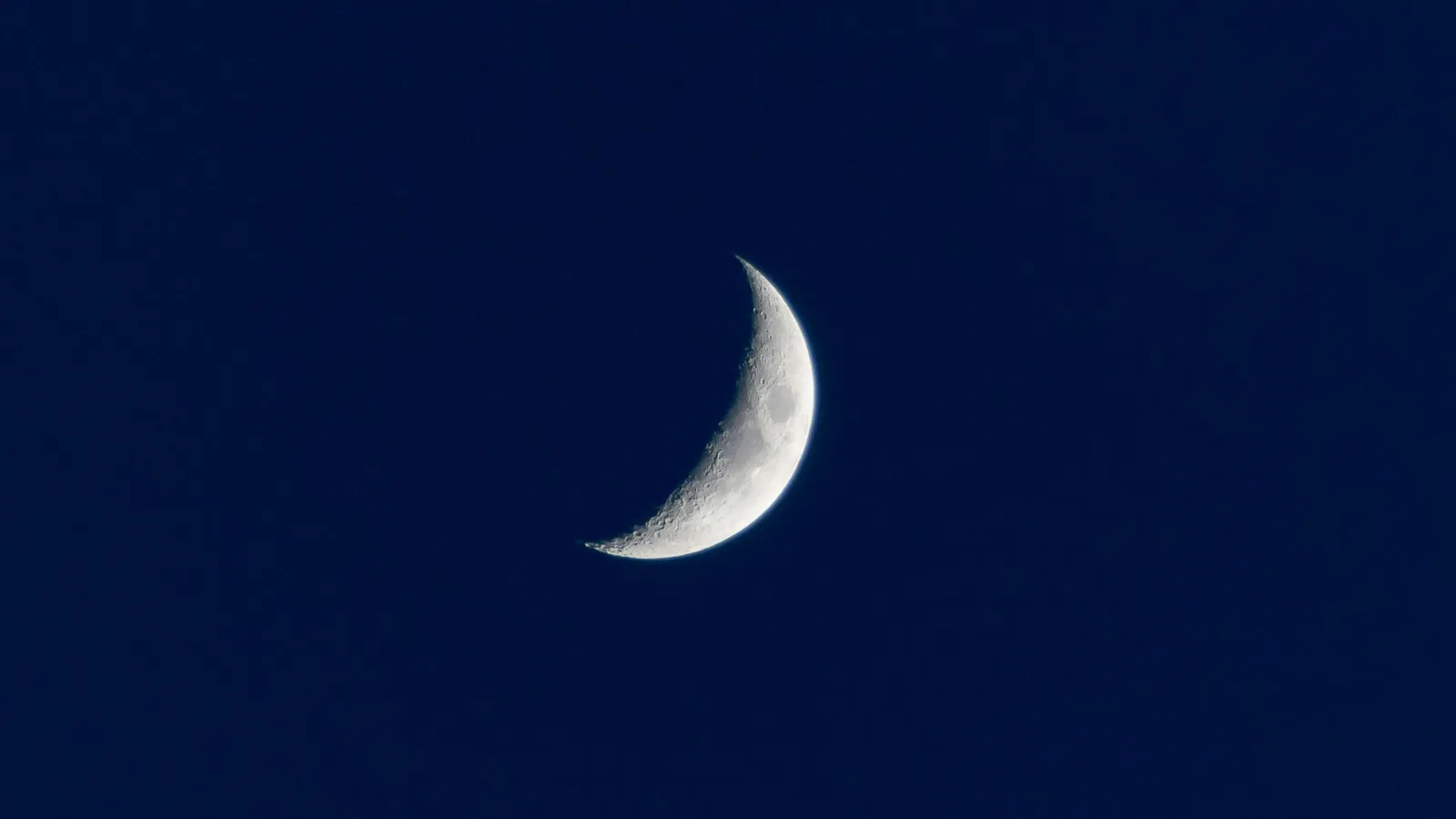 A thin crescent Moon in a dark blue sky