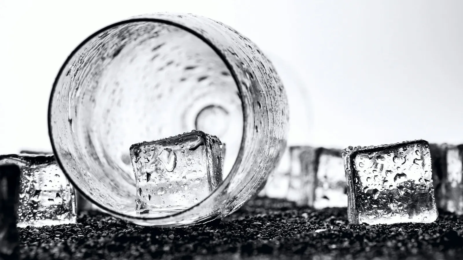 A tipped-over glass with ice cubes beside it on a white surface
