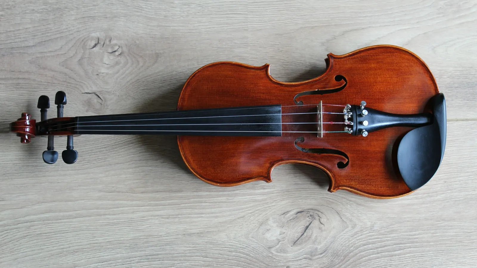 A violin lying on a pale wooden surface
