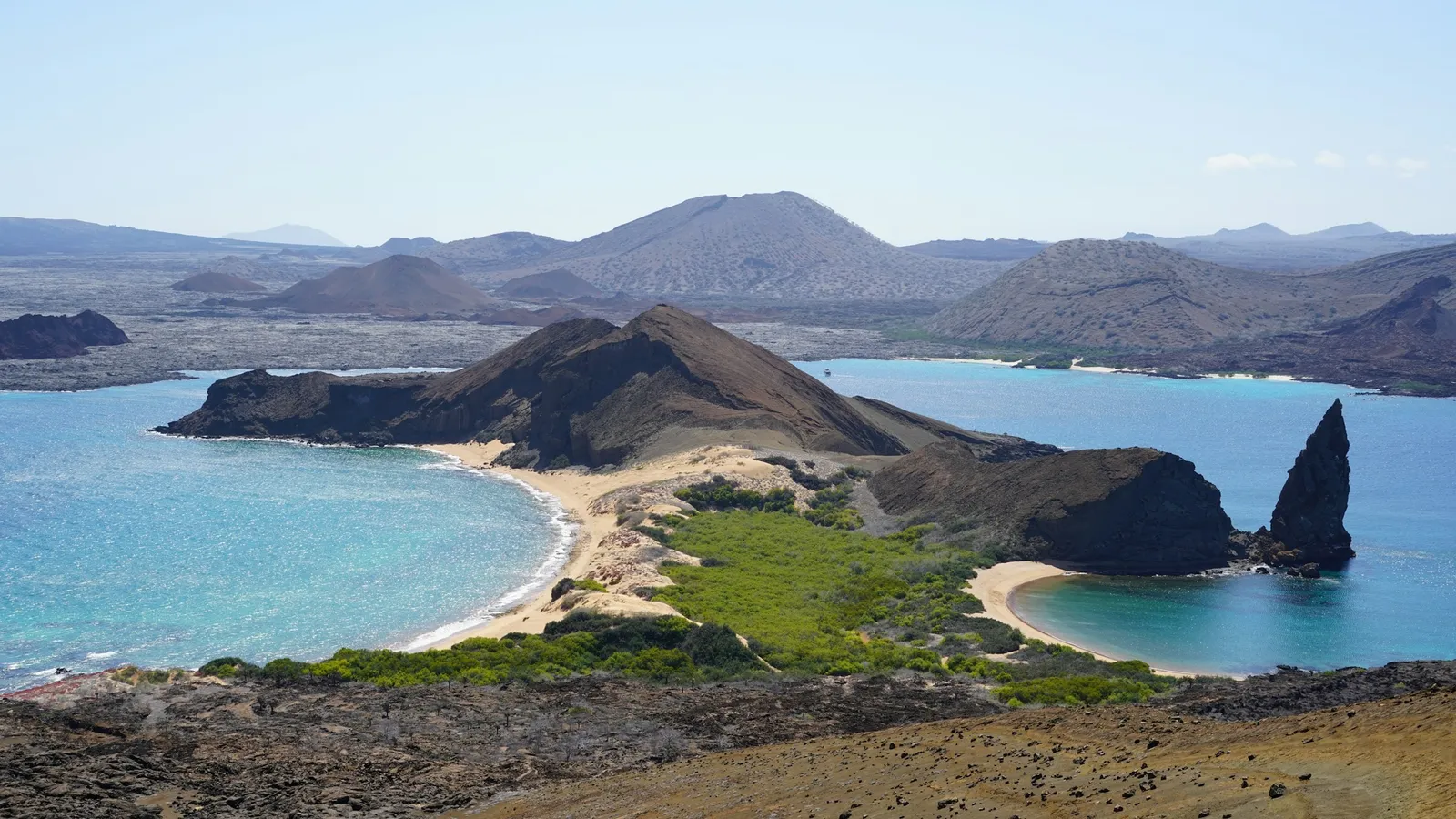 A volcanic island coastline with turquoise bays and a tall rock spire