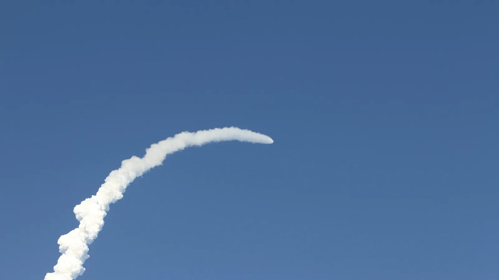 A white launch trail rising into a blue sky