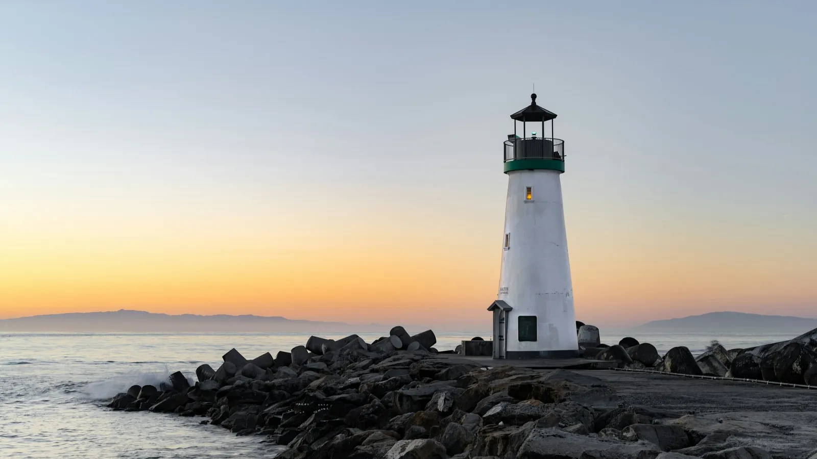 A white lighthouse on a rocky shore at sunset
