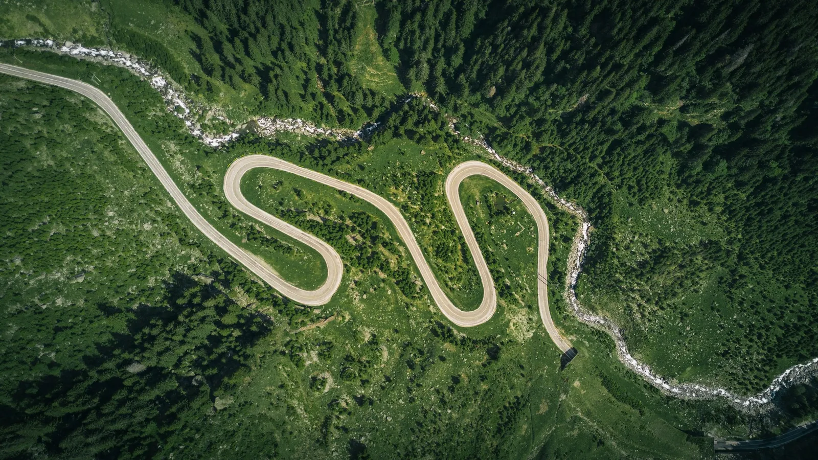 A winding road curving across green hills from above