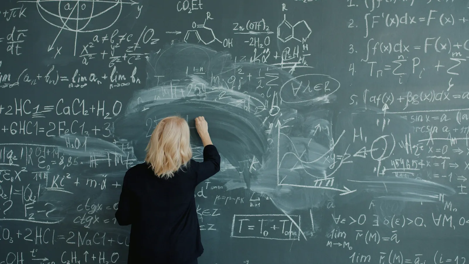 A woman writing equations on a large chalkboard
