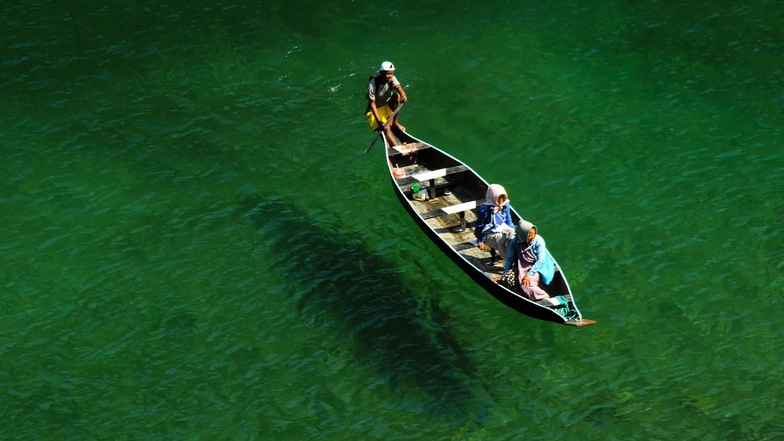 A wooden boat crossing a green river, seen from above
