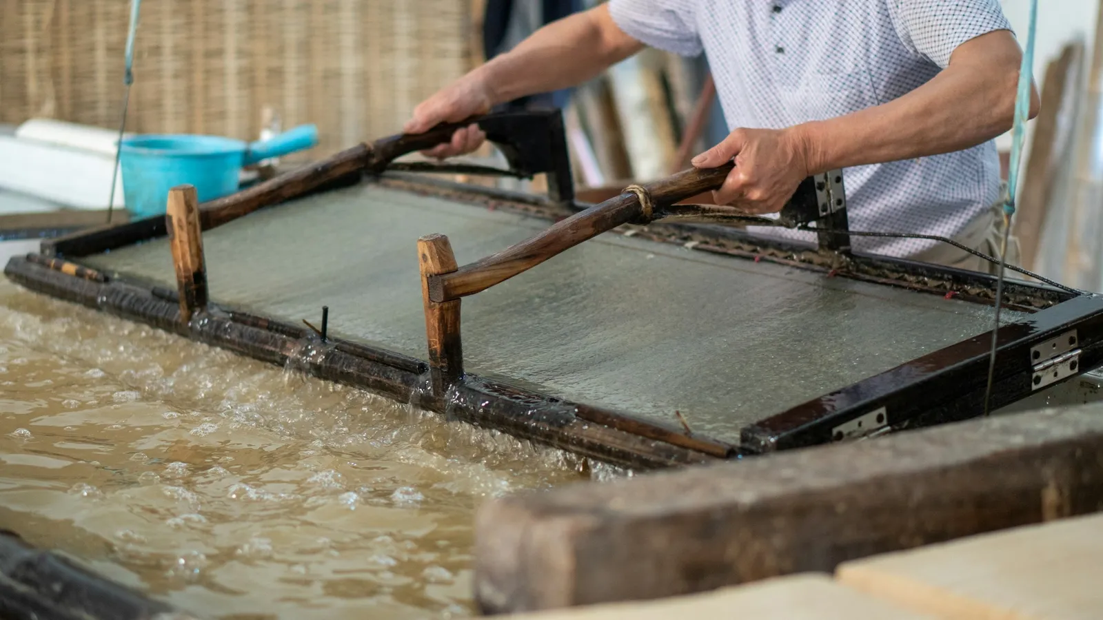 A worker lifting a mould from a vat to make paper by hand