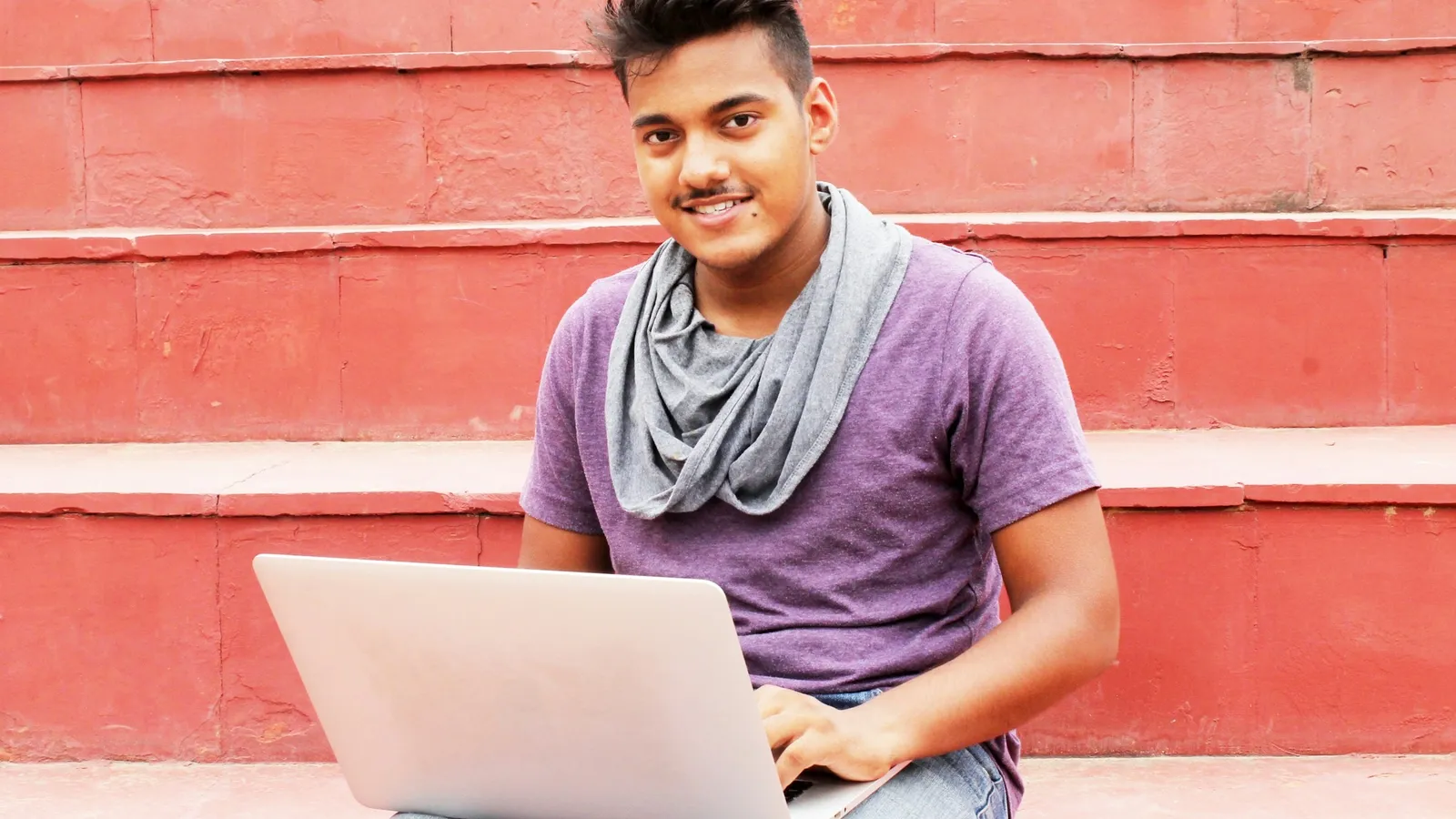 A young man sitting on red steps with a laptop on his lap