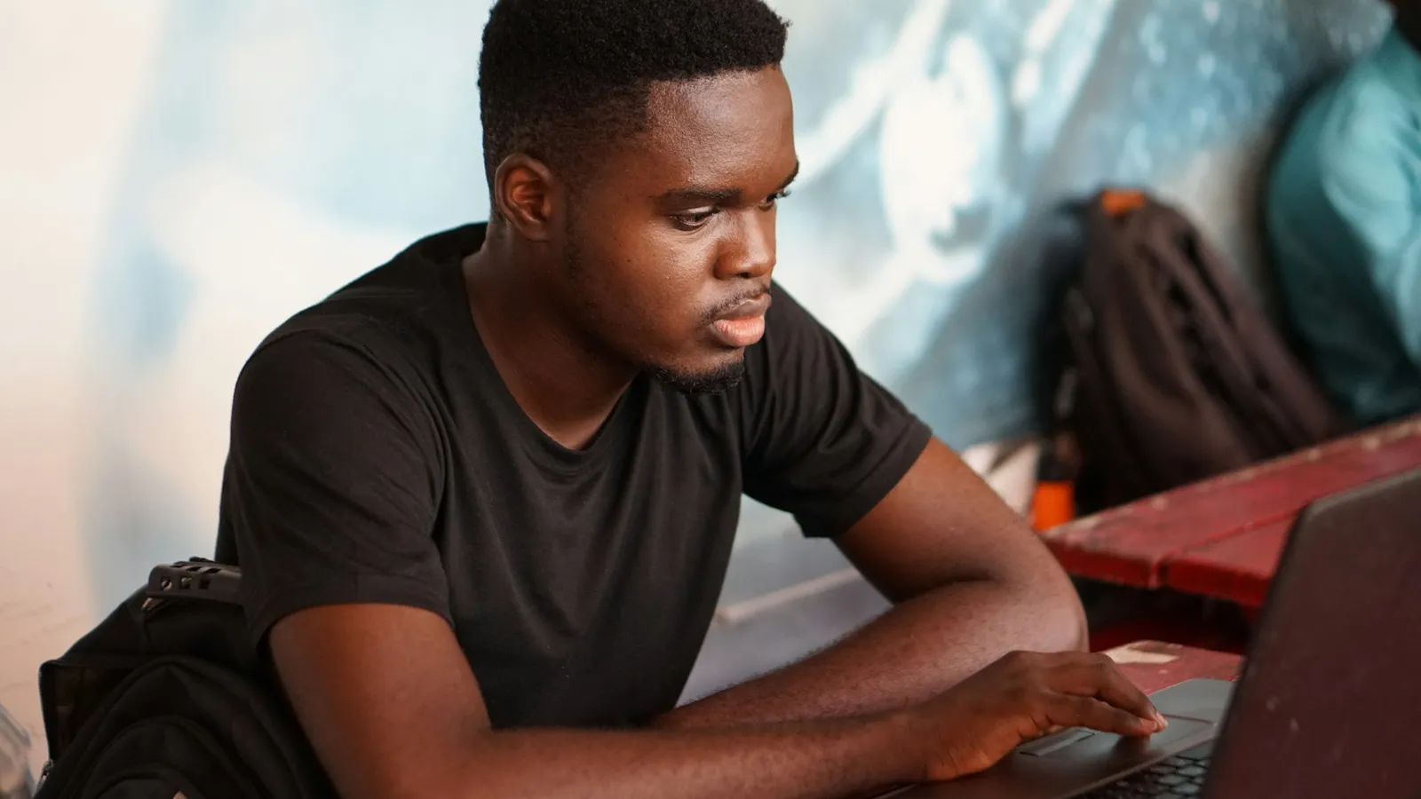 A young man studies intently at a laptop at a classroom desk