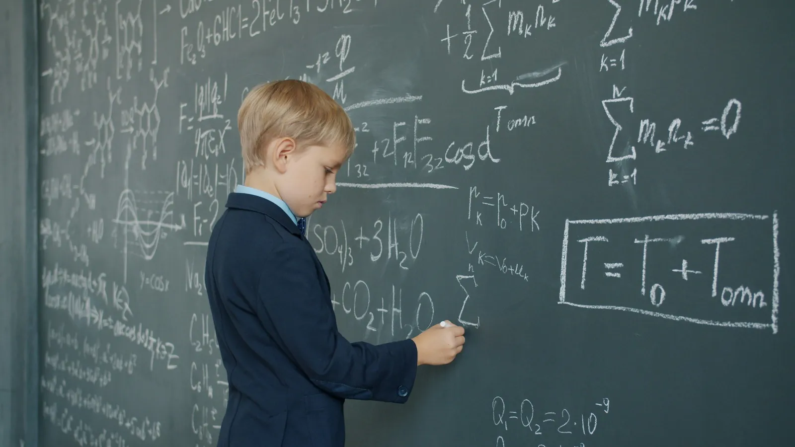 A young student writing equations on a large chalkboard