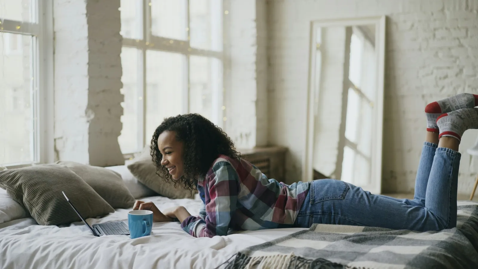 A young woman lying on a bed working on a laptop