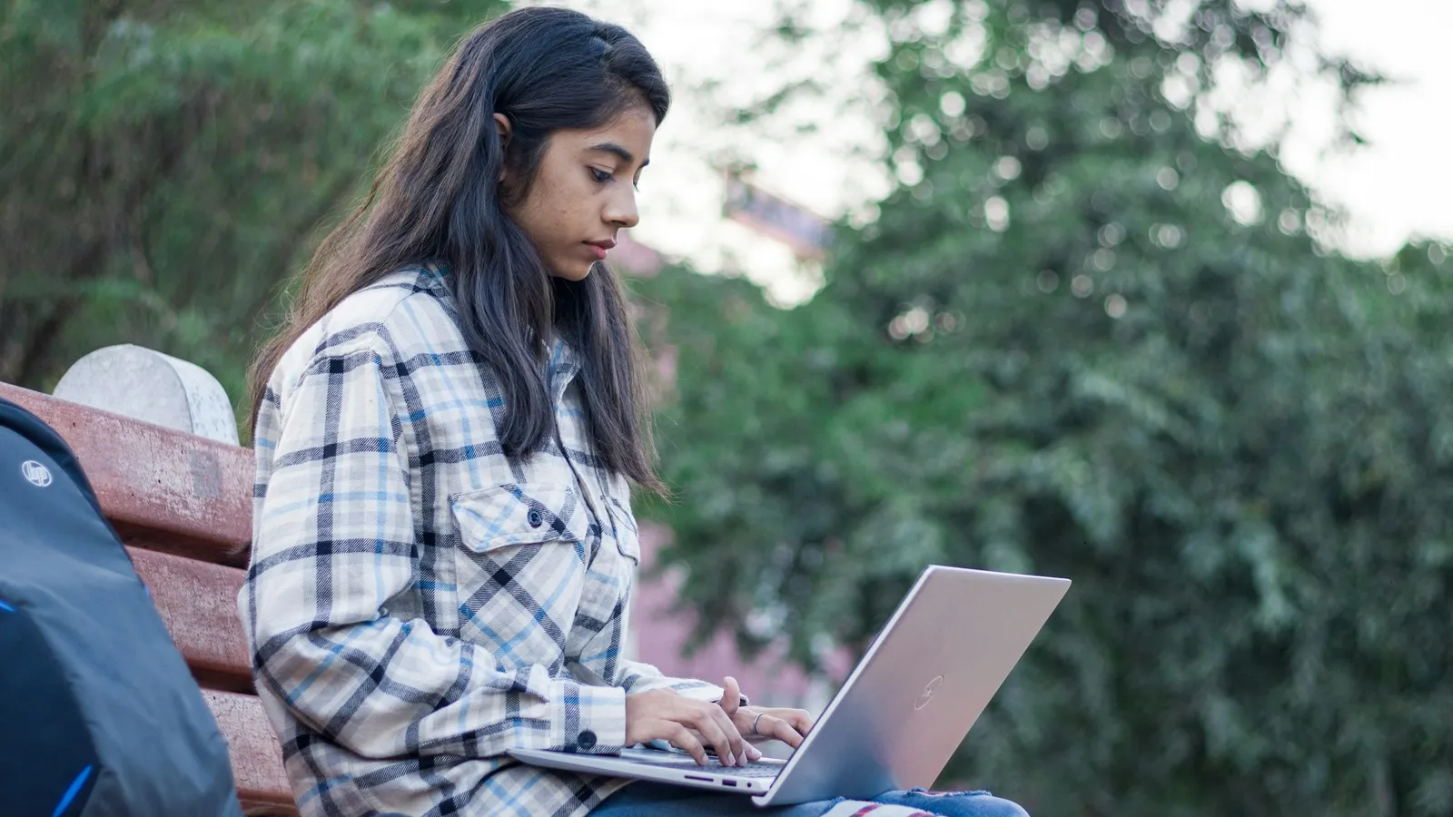A young woman working on a laptop on a park bench
