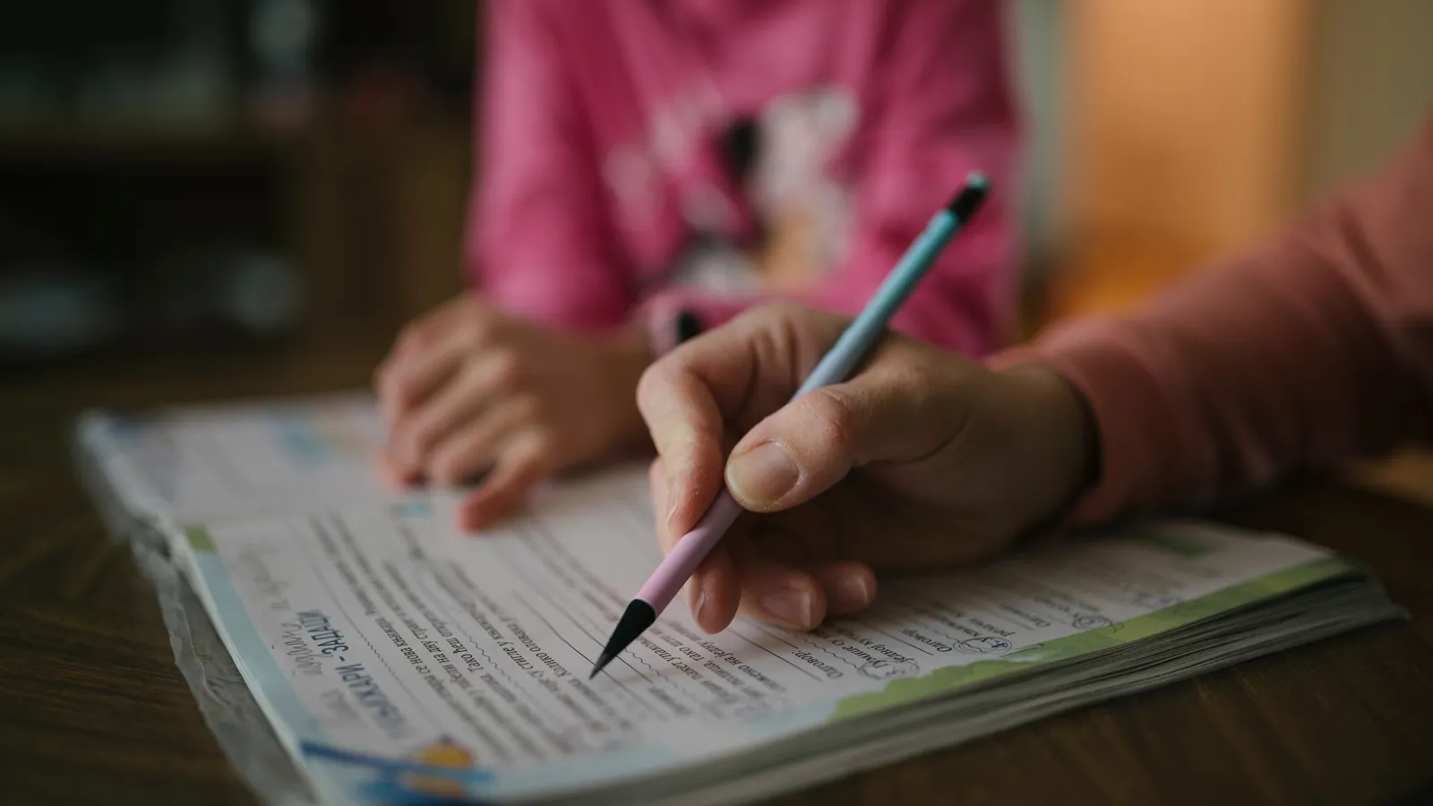 Adult guiding a child writing with a pencil at a table