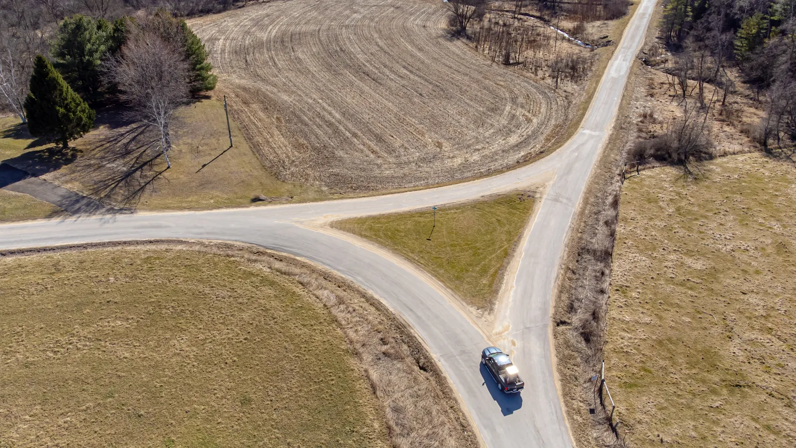 Aerial view of a country road splitting into two paths between fields, with a car at the fork